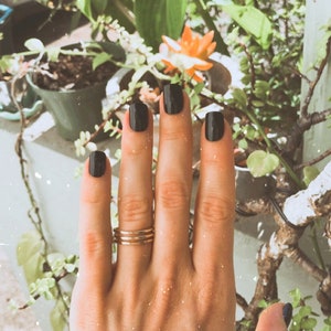 May include: A hand with black nail polish and a gold ring on the ring finger.