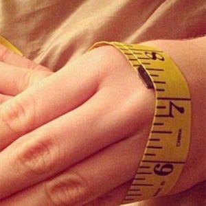 May include: A yellow measuring tape wrapped around a wrist, showing measurements in inches. The tape is marked with black numbers and lines, indicating a measurement of approximately 6.5 inches.