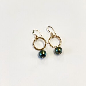 May include: A pair of gold hoop earrings with a black pearl dangling from each hoop.