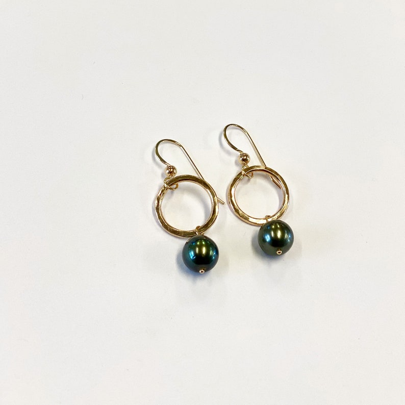 May include: A pair of gold hoop earrings with a black pearl dangling from each hoop.