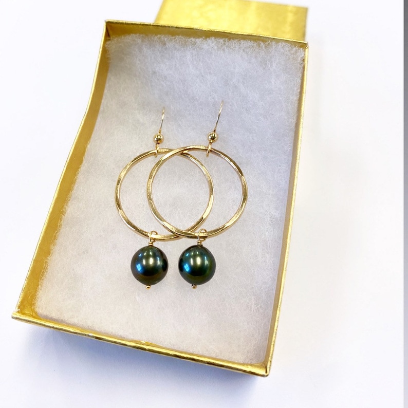 May include: Gold hoop earrings with a dark green pearl dangling from each hoop.