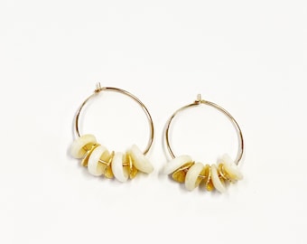 May include: Gold hoop earrings with white shell beads. The earrings are simple and elegant, perfect for everyday wear.