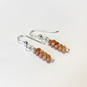 May include: A pair of silver dangle earrings with a graduated row of small, round, speckled, peach-colored beads.