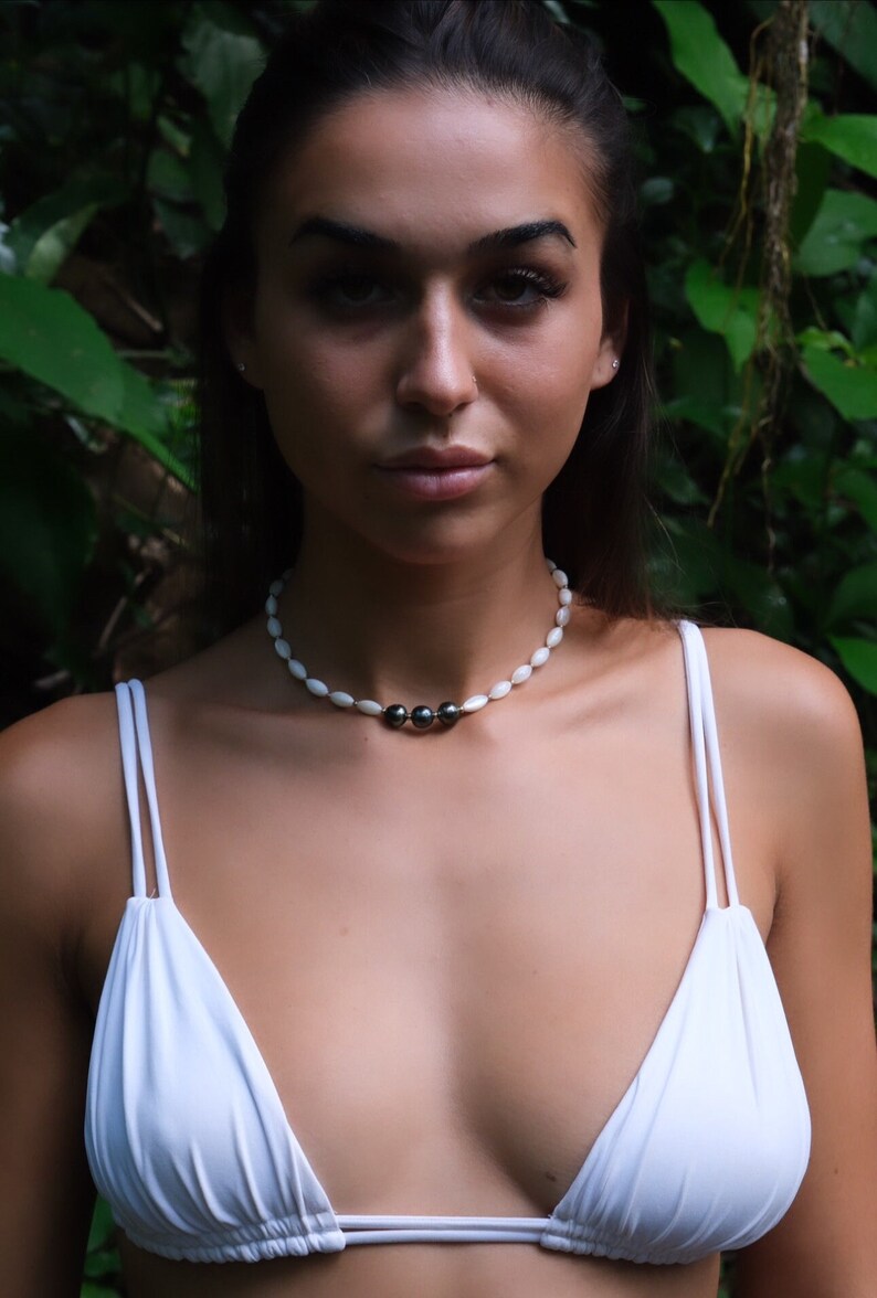 Op de afbeelding: Een vrouw draagt een wit bikini top met een witte en zwarte parelketting. De ketting heeft drie zwarte parels in het midden.