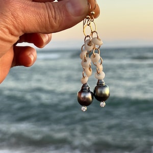 May include: Gold-toned earrings featuring a combination of small, white shell beads and dark gray, pear-shaped pearls. Each pearl has a small, sparkling accent at the base. The earrings are suspended from gold hoops.