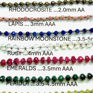 May include: A collection of eleven horizontal strands of faceted gemstone beads, each labeled with its name and size. The strands include black spinel, pink silverite, gold pyrite, rhodocrosite, lapis, rainbow moonstone, ruby, emeralds, peridot, carnelian, and amethyst.