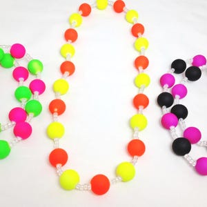 May include: Three beaded necklaces featuring round, matte-finish silicone beads strung on clear cord. One necklace has neon green and pink beads, one has neon yellow and orange beads, and one has alternating black and bright pink beads.