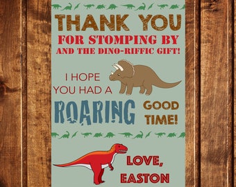 May include: A green thank you card with a brown wooden background. The card features a dinosaur theme with the text "THANK YOU FOR STOMPING BY AND THE DINO-RIFFIC GIFT! I HOPE YOU HAD A ROARING GOOD TIME! LOVE, EASTON".