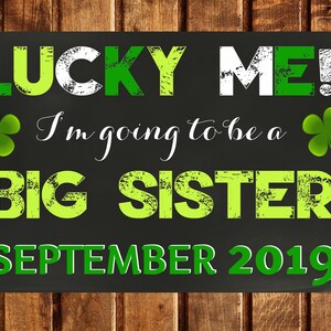 Puede incluir: Un letrero de pizarra negra con acentos de trébol verde que anuncia "Lucky Me! I'm going to be a Big Sister September 2019."