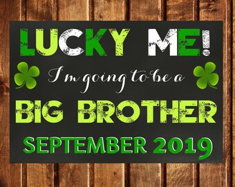 May include: A black chalkboard with green shamrocks and the text "LUCKY ME! I'm going to be a BIG BROTHER SEPTEMBER 2019".