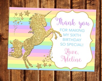 May include: A thank you card with a gold glitter unicorn silhouette on a rainbow striped background. The text reads "Thank you for making my sixth birthday so special! Love, Adeline".