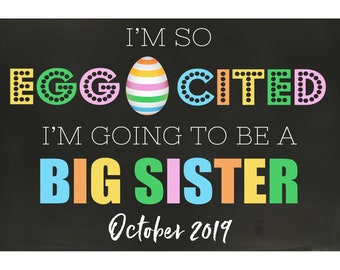 Könnte beinhalten: Eine schwarze Tafel mit dem Text "I'm so EGG-CITEd I'm going to be a BIG SISTER October 2019". Die Buchstaben sind in verschiedenen Farben gehalten und haben weiße Punkte um sie herum. In der Mitte des Textes befindet sich ein buntes, gestreiftes Ei.