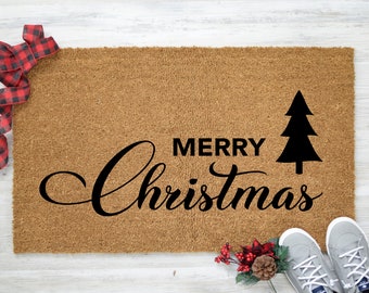May include: A brown coir doormat with the text "Merry Christmas" in black cursive lettering and a black silhouette of a Christmas tree.