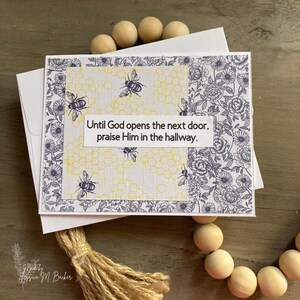 May include: A white card with a floral design and a yellow honeycomb pattern. The card has the text "Until God opens the next door, praise Him in the hallway."