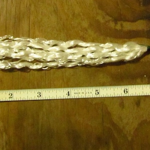 May include: A cream-colored tassel with a metal swivel clasp, measuring approximately 9 inches in length. The tassel is made of looped, woven material. A ruler is placed next to the tassel for scale.