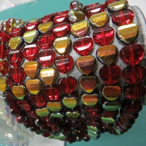 May include: A close-up of a strand of red and gold heart-shaped beads. The beads are iridescent and have a shiny finish.