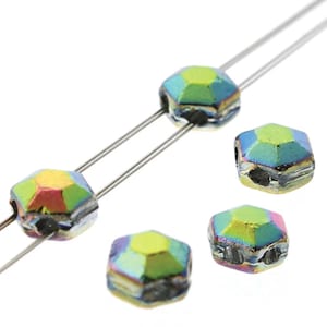 May include: Close-up of iridescent faceted beads in various sizes. The beads have a hexagonal shape with multiple facets that reflect a spectrum of colors, including green, yellow, and blue. Two beads are strung on a thin, silver wire.