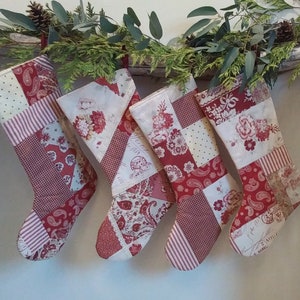 May include: Four patchwork Christmas stockings hanging in a row, each crafted from various red and white fabric patterns including paisley, floral, polka dot, and gingham prints. The stockings feature intricate stitching and varied textile designs.