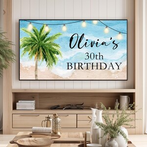 May include: A digital display with a beach scene and the text "Olivia's 30th Birthday" with string lights hanging above.