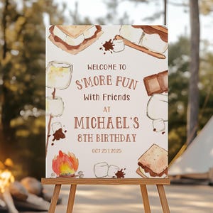 Könnte beinhalten: Eine Holzstaffelei zeigt ein Schild mit dem Text "Welcome to S'more Fun with Friends at Michael's 8th Birthday". Das Schild zeigt Aquarellillustrationen von S'mores, Marshmallows und einem Lagerfeuer. Ein Zelt und ein Lagerfeuer befinden sich im Hintergrund.