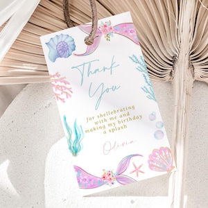 May include: A rectangular mermaid-themed thank you tag with a brown string. The tag features the words "Thank You" in cursive, along with aquatic illustrations and the text "for shellebrating with me and making my birthday a splash".