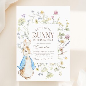 May include: A white invitation card featuring a watercolour illustration of a bunny in a blue jacket, surrounded by a floral wreath. The text reads "A cute little bunny is turning one!" with event details. Ideal for a first birthday.