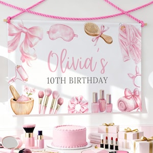 Könnte beinhalten: Ein rosa-weißes Banner mit der Aufschrift "Olivia's 10th Birthday" hängt über einem Tisch mit Schönheitsprodukten. Auf dem Tisch befinden sich ein rosa Kuchen, Make-up und verpackte Geschenke. Ballons sind im Hintergrund zu sehen.