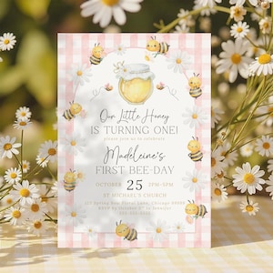 The Printable Occasions offers custom wedding birthday and baby shower templates for every celebration. Pink first birthday bee invitation for girls with watercolor bumblebees, honey jar, daisies, and pink gingham border. Shown among white daisies with soft sunlight. Editable Canva design in pink color scheme for a girl’s bee day celebration.