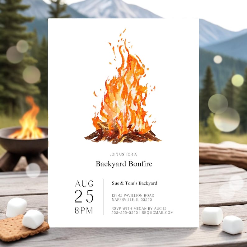 Editable backyard bonfire invitation featuring a large watercolor campfire illustration with warm orange and golden flames. The simple white design includes modern black typography with customizable party details. The invitation is displayed outdoors on a rustic wood table with mountains and evergreen trees in the background. A glowing fire pit and scattered marshmallows create a cozy campfire party setting.