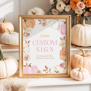Printable pumpkin birthday sign shown in a vintage gold frame placed on a white dresser. Surrounded by small pumpkins in white and peach, dried florals, and soft sunlight. The design includes pink and cream pumpkins with watercolor floral accents, perfect for a fall birthday party or harvest celebration.