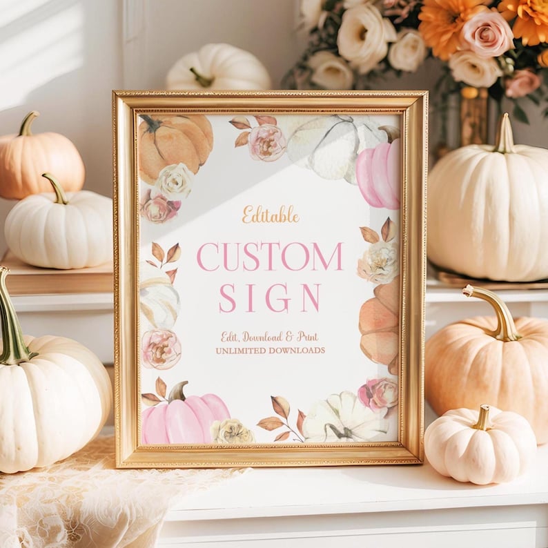 Printable pumpkin birthday sign shown in a vintage gold frame placed on a white dresser. Surrounded by small pumpkins in white and peach, dried florals, and soft sunlight. The design includes pink and cream pumpkins with watercolor floral accents, perfect for a fall birthday party or harvest celebration.