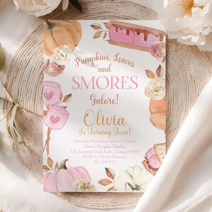 Girls Fall Smores Birthday Invitation template centered on a woven charger beneath flowing ivory fabric that naturally frames the design from each side. Soft white peonies and gentle sunlight create an airy, romantic autumn setting while the watercolor pumpkins, blush marshmallows, toasted smores, and autumn leaves stand out beautifully. Editable Canva birthday invitation for a pumpkin themed party.