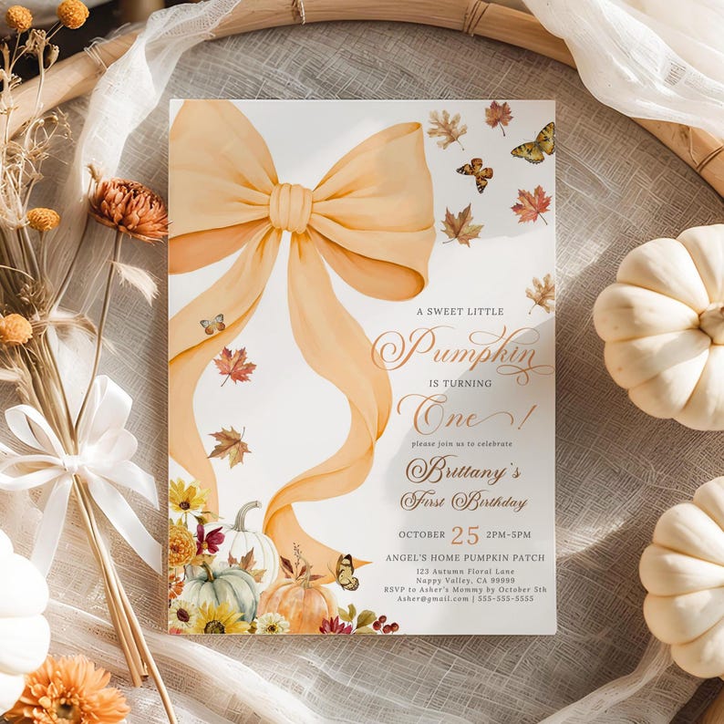 Flat lay of pastel pumpkin and coquette bow birthday invitation for girls featuring watercolor pumpkins, autumn leaves, sunflowers, and butterflies, styled in a wicker tray surrounded by rustic fall decor. Perfect for an elegant autumn first birthday celebration, cozy pumpkin patch party, or coquette-themed fall birthday with personalized details.