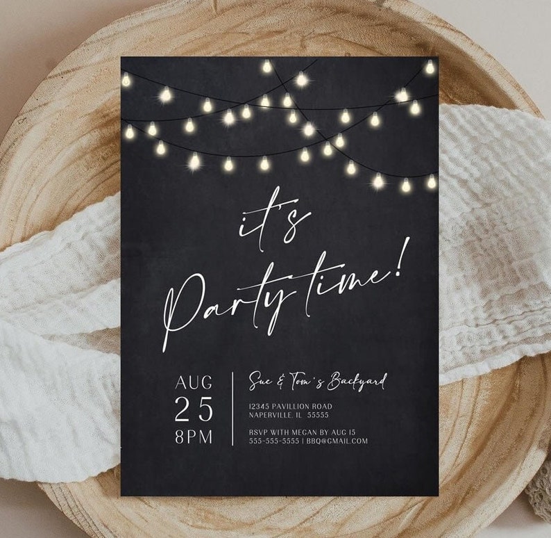 Modern adult party invitation featuring warm string lights against a black background with elegant white script typography. Date, time, location and RSVP information are arranged neatly along the bottom of the design. The printed invitation rests on a round natural wood surface with soft neutral fabric surrounding it. A versatile design for men's or women's birthdays and evening parties.