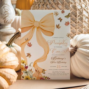 Pastel pumpkin first birthday invitation featuring a large watercolor orange bow, soft pastel pumpkins, autumn leaves, butterflies, and elegant script text, styled upright among cream and orange pumpkins with a woven basket background. Perfect for a girl’s fall birthday party, rustic pumpkin patch celebration, or coquette-inspired autumn gathering with customizable details.