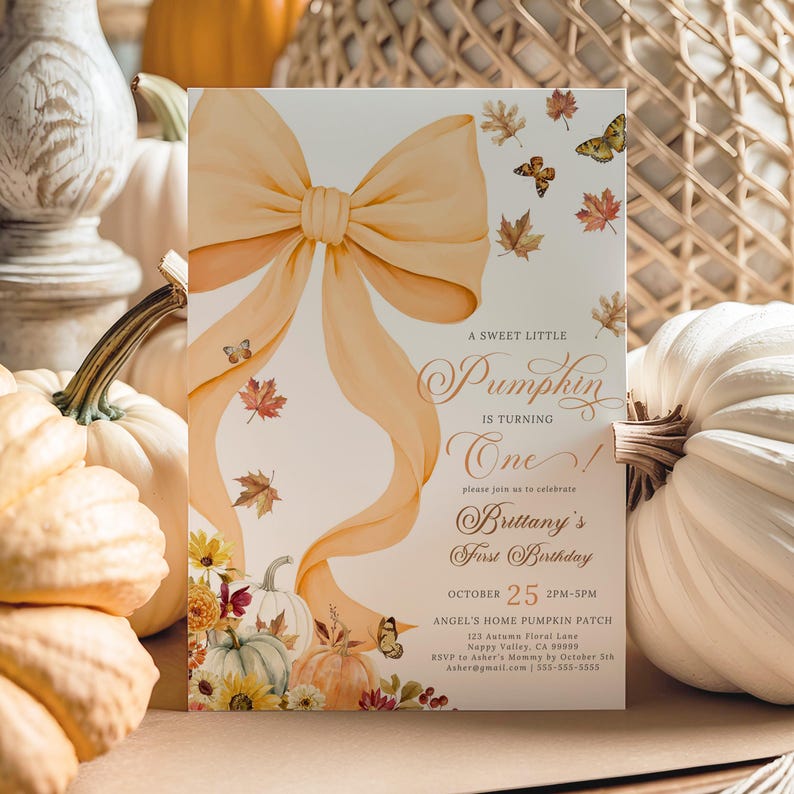 Pastel pumpkin first birthday invitation featuring a large watercolor orange bow, soft pastel pumpkins, autumn leaves, butterflies, and elegant script text, styled upright among cream and orange pumpkins with a woven basket background. Perfect for a girl’s fall birthday party, rustic pumpkin patch celebration, or coquette-inspired autumn gathering with customizable details.