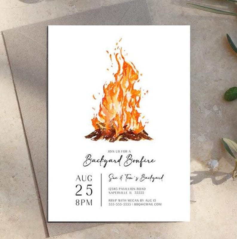 Bonfire party invitation template with a hand painted watercolor fire illustration and simple black party details. The design includes space for the date, time, backyard location and RSVP information. The printed invitation rests on a neutral stone surface with subtle greenery nearby. The natural setting complements a casual backyard bonfire, barbecue or outdoor party.