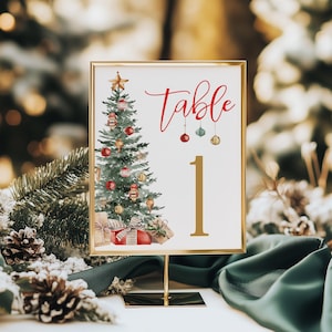 May include: A gold-framed table number card featuring a watercolour Christmas tree illustration. The word "Table" is in red script, and the number "1" is in gold. Ornaments and gifts are also depicted.
