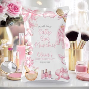 Może przedstawiać: Różowa i biała torba na przyjęcie z napisem "Please Enjoy Salty Spa Munchies" i "Olivia's 10th Birthday". Torba jest ozdobiona ilustracjami w tematyce spa i produktami kosmetycznymi.