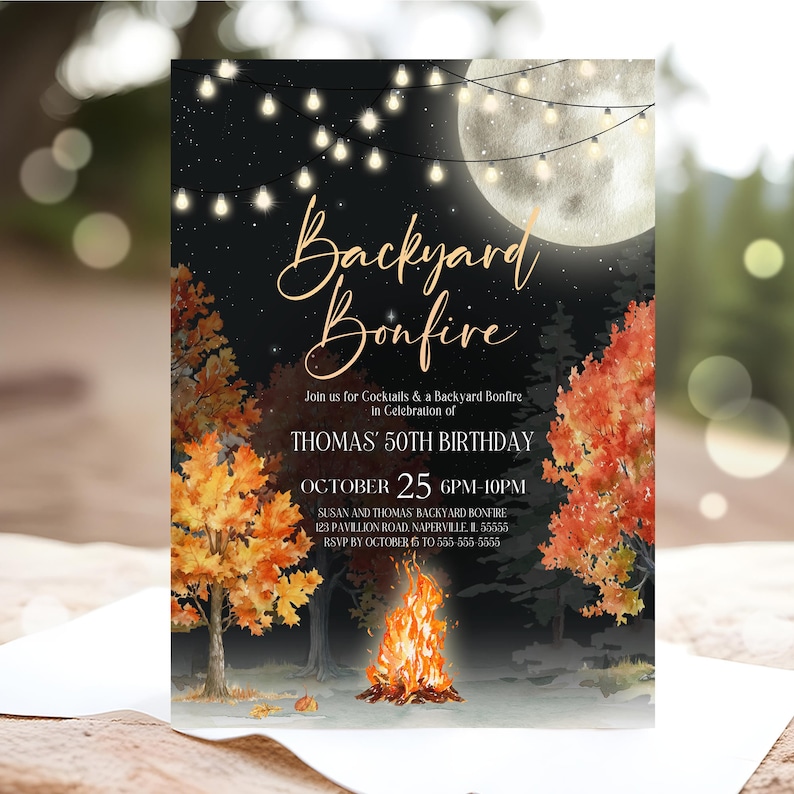 Autumn backyard bonfire invite features warm fire glow, full moon, café lights, and rich fall trees framing the design. Script and serif fonts combine for an elegant adult birthday look. Invitation is placed on soft neutral fabric with antler decor and dried leaves around it. Earthy textures and warm tones create a seasonal rustic tabletop display.