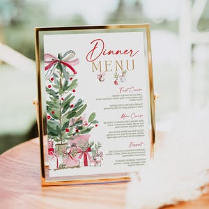 May include: A vertical dinner menu card in a gold metal frame featuring a watercolor illustration of a Christmas tree with red bows and gifts. The text reads Dinner Menu, First Course, Main Course, and Dessert with various food items listed.