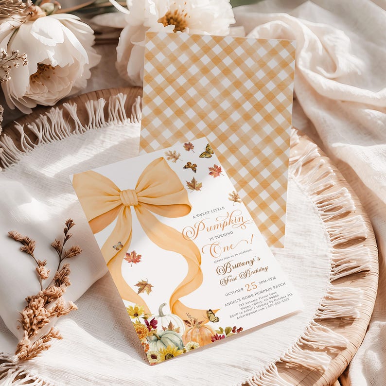Editable pastel pumpkin birthday invitation for girls with a soft orange bow, watercolor pumpkins, fall florals, and butterflies, displayed alongside a matching gingham backside design. Styled flat on textured white fabric with neutral flowers and boho rustic fall decor, perfect for an elegant autumn pumpkin patch birthday or first birthday celebration invitation.