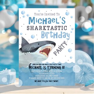 Puede incluir: Una invitaci&oacute;n de fiesta de cumplea&ntilde;os azul y blanca con una ilustraci&oacute;n de tibur&oacute;n de dibujos animados. La invitaci&oacute;n dice "You're Invited To Michael's Sharktastic Birthday Party". Tambi&eacute;n incluye la fecha, la hora y la ubicaci&oacute;n de la fiesta.