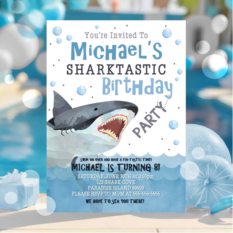 Puede incluir: Una invitaci&oacute;n de fiesta de cumplea&ntilde;os azul y blanca con una ilustraci&oacute;n de tibur&oacute;n de dibujos animados. La invitaci&oacute;n dice "You're Invited To Michael's Sharktastic Birthday Party". Tambi&eacute;n incluye la fecha, la hora y la ubicaci&oacute;n de la fiesta.
