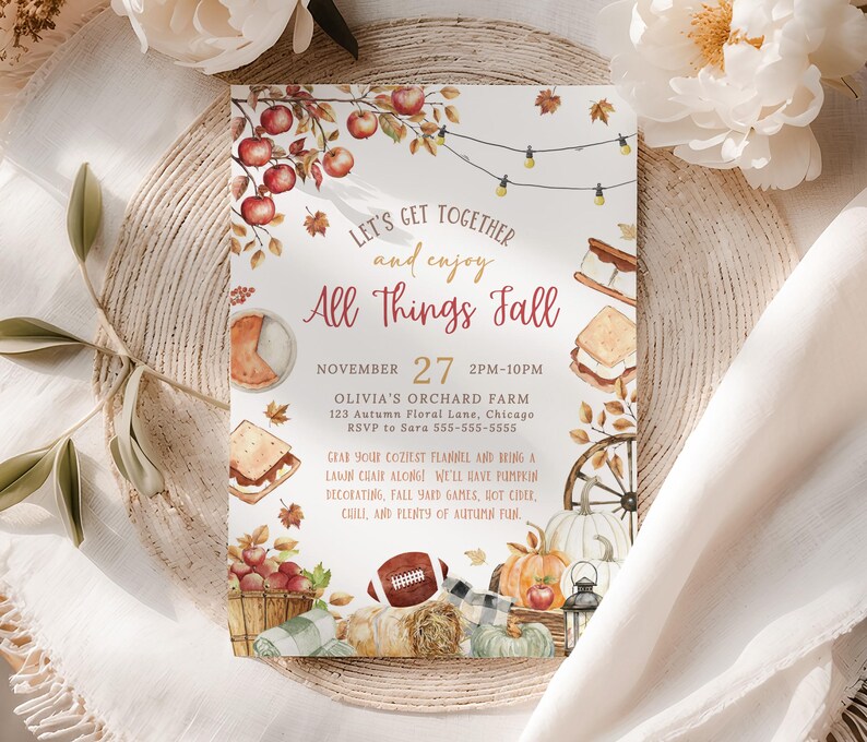 Seasonal fall festival invitation design with watercolor pumpkins, apples, hay bale, lantern and autumn leaves surrounding the party wording in warm harvest colors. The center text area allows customization of date, location and event details. The card is displayed upright with soft pumpkins, dried florals and warm fall tones in the background creating a cozy autumn gathering scene.