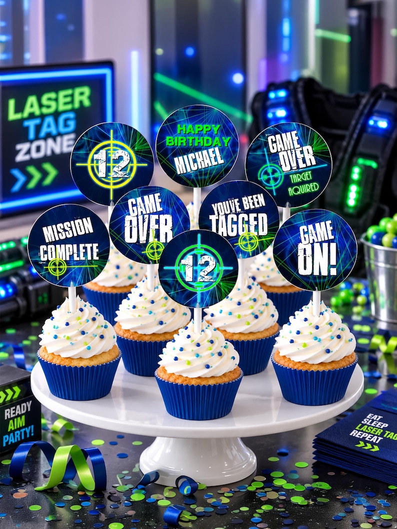 May include: A set of round cupcake toppers featuring laser tag themes with text including "12", "Happy Birthday Michael", "Game Over", "Mission Complete", "You've Been Tagged", and "Game On!" displayed on cupcakes with white frosting and blue liners.