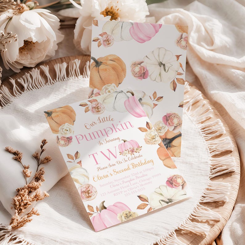 The Printable Occasion offers a girl’s second birthday invitation with a pink pumpkin theme. The design features watercolor pumpkins, blush florals, and autumn leaves with the wording “Our Little Pumpkin is Turning Two.” Editable in Canva, this fall birthday invitation is shown in a flatlay on a rustic woven tray with white fringe linen, flowers, and natural light styling.