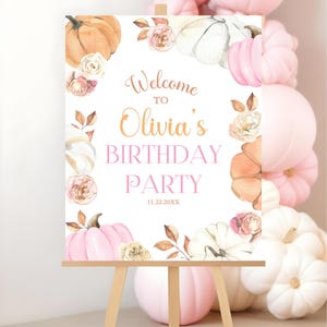Editable welcome sign for a pumpkin first birthday party featuring pink white and orange pumpkins with roses and fall leaves personalized with the child’s name and displayed on an easel surrounded by pastel pink balloons for a soft and feminine autumn birthday celebration entrance decor for a little girl’s party