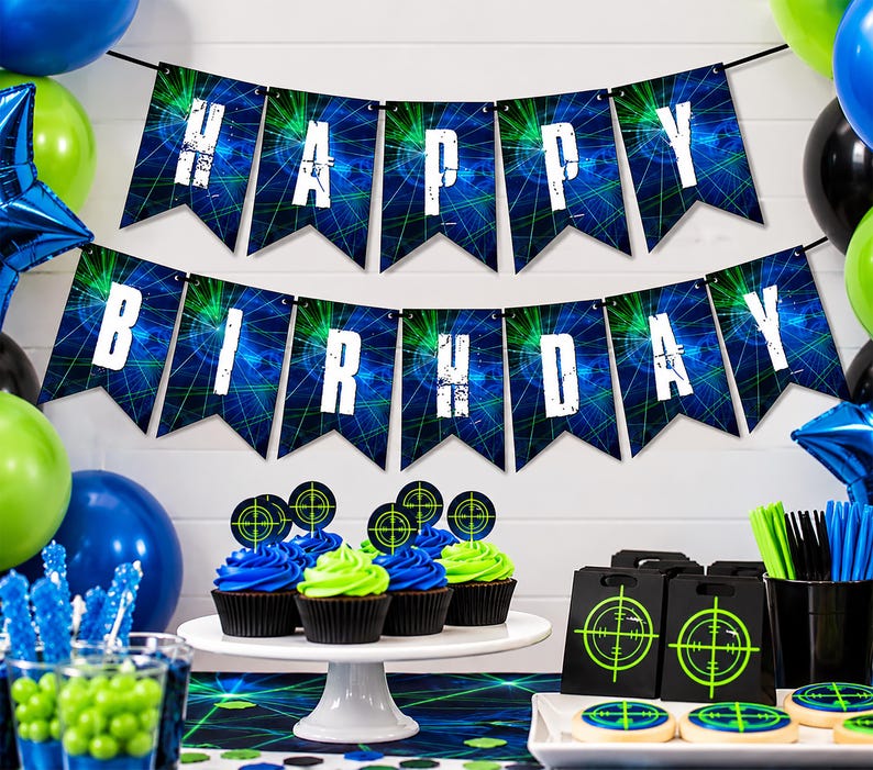Laser tag birthday banner is displayed above a colorful party table with bright blue, neon green and black decorations. The 5x7" pennants spell Happy Birthday in bold distressed white lettering over glowing blue and green laser graphics. You've Been Tagged end pieces feature coordinating neon target designs. Balloons, cupcakes and gamer party decorations complete the laser tag birthday setup.