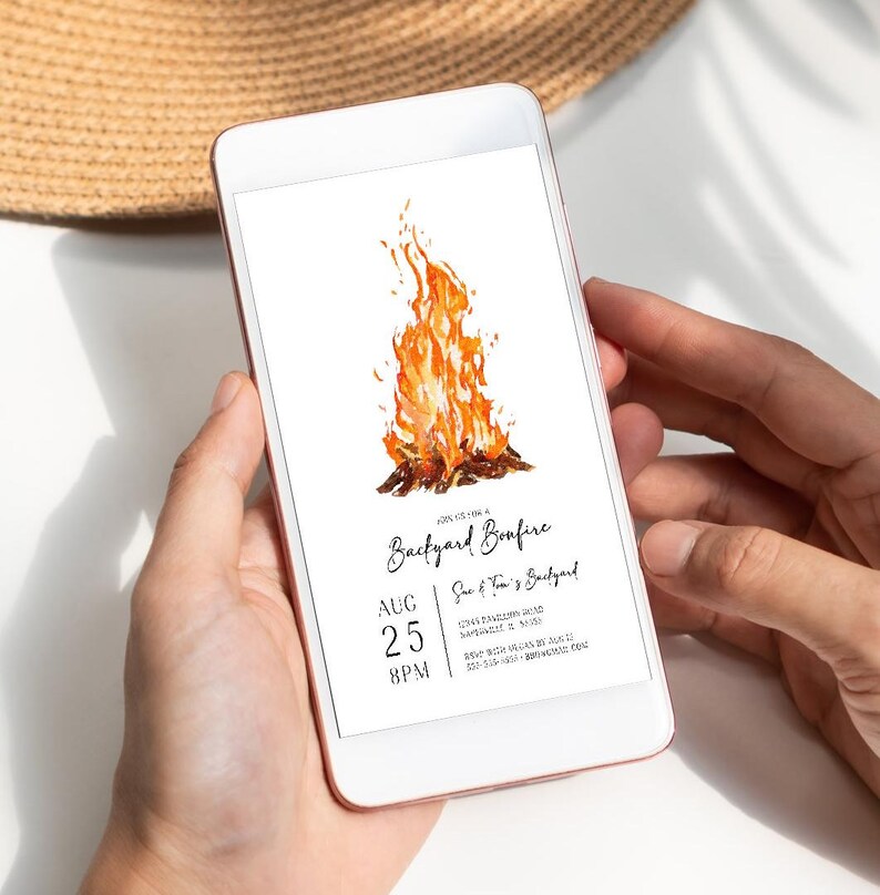 Digital bonfire party invitation displayed on a smartphone with a bright watercolor campfire and modern black lettering. The invitation includes customizable date, time, location and RSVP details for a backyard gathering. The phone is held in hand against a bright neutral background with soft natural shadows. Ideal for sharing a bonfire birthday, outdoor party or backyard bonfire invitation digitally.